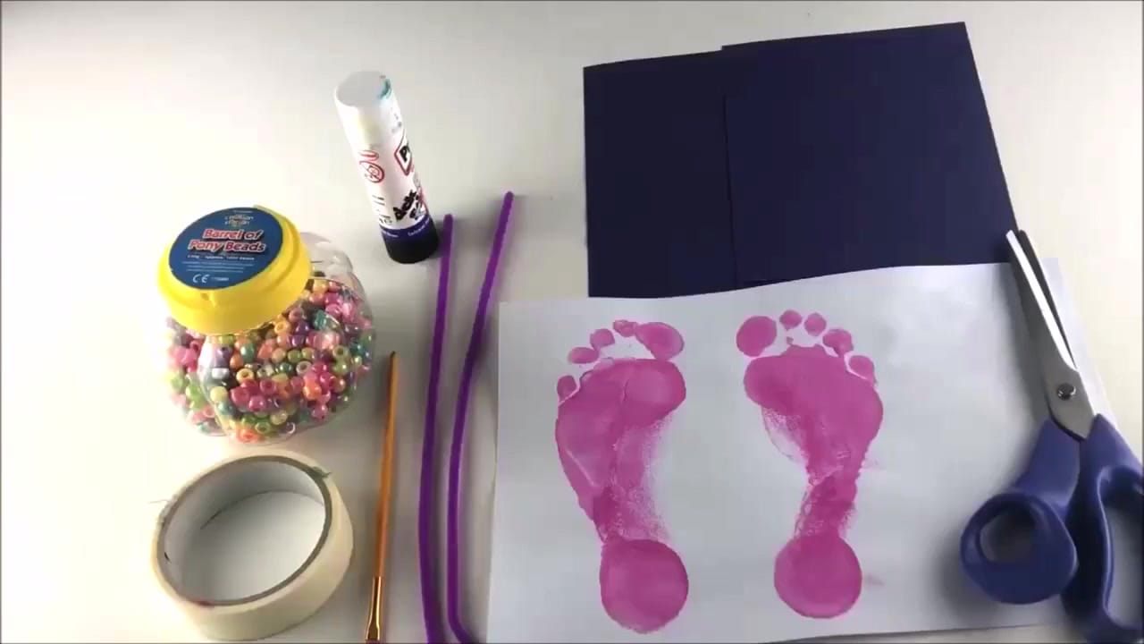 Painted footprints drying on white card – close-up of two bright painted footprints ready to be cut out for a beaded flip flop craft.