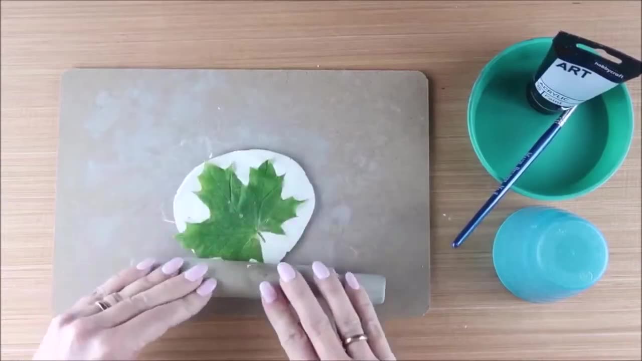 A green leaf being gently rolled into the clay to create a clear imprint.