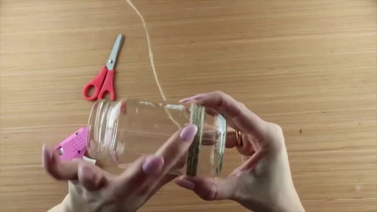 Hands applying glue to the top edge of the jar and beginning to wrap string around it
